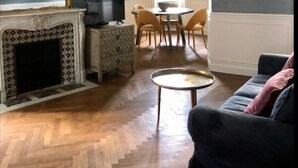 Una sala de estar con chimenea, una araña, un sofá y una zona de comedor con sillas y una mesa.