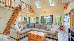 A spacious living room with a large sectional sofa, a wooden coffee table, and a staircase leading to an upper level. - Port Orchard Lakefront Cabin w/ Fire Pit & Grill! (Port Orchard)