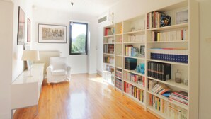 Une pièce spacieuse dotée d’un plancher en bois, d’une chaise blanche, d’un bureau avec une lampe et d’une grande bibliothèque remplie de livres.
