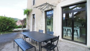 Une terrasse extérieure avec une table et des chaises, un banc et une fenêtre donnant sur les environs.