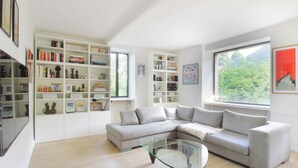 Un salon moderne avec un canapé d’angle, une table basse en verre et des étagères intégrées remplies de livres et d’objets décoratifs.