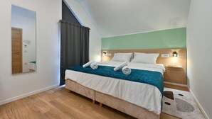 Moderni hotellihuone, jossa on sänky, yöpöytävalaisimet, peili ja puulattia.