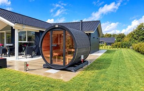 Una casa moderna con una gran estructura cilíndrica, posiblemente una sauna o bañera de hidromasaje, adosada al edificio principal.