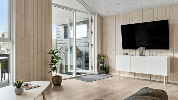 A modern living room with a large TV, wooden panel walls, a sliding glass door leading outside, and a dining area with a table and chairs. - Awesome home in Tarm with WiFi (Tarm)