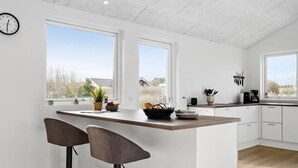 A modern kitchen with white cabinets, a wooden island, two bar stools, and large windows offering a view of the outdoors. - Awesome home in Tarm with WiFi (Tarm)