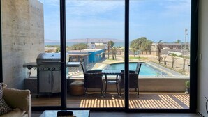 Een balkon met een barbecue, zwembad en terrasmeubilair.