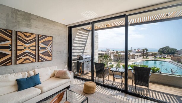 Een moderne woonkamer met een groot raam, een bank, een bijzettafeltje en een barbecue.
