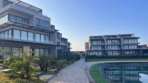 A modern building complex with multiple floors, a gravel pathway, and a water feature.