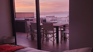 A balcony with wicker chairs and a table, overlooking a body of water and distant hills.