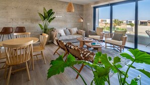 A modern living room with a large window, a sofa, a coffee table, and a dining area with chairs. - Cozy flat w/ Balcony View on the Lagoon, 5min from Kite Point & National Reserve (Paracas)