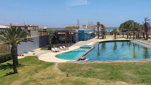 A modern pool area with a clear view of the sea, a covered patio, and a grassy lawn. - Cozy flat w/ Balcony View on the Lagoon, 5min from Kite Point & National Reserve (Paracas)