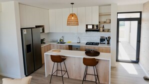 A modern kitchen with white cabinets, a stainless steel refrigerator, a central island with stools, and a hanging pendant light. - Cozy flat w/ Balcony View on the Lagoon, 5min from Kite Point & National Reserve (Paracas)