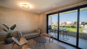 A modern living room with a sofa, chairs, a coffee table, and a large sliding glass door leading to an outdoor patio with a table and chairs. - Cozy & Classy flat in Paracas Bay with Balcony View on the Saltwater Lagoon (Paracas)