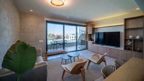 A modern living room with a large TV, comfortable seating, and a view of the city through large windows. - Cozy & Classy flat in Paracas Bay with Balcony View on the Saltwater Lagoon (Paracas)