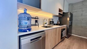 A modern kitchen with a dishwasher, a large water dispenser, a sink, a coffee maker, and a stainless steel refrigerator. - Cozy & Classy flat in Paracas Bay with Balcony View on the Saltwater Lagoon (Paracas)