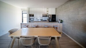 A modern kitchen with white cabinets, a central island with bar stools, and a large wooden dining table with chairs. - Cozy & Classy flat in Paracas Bay with Balcony View on the Saltwater Lagoon (Paracas)