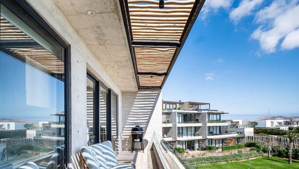 Un balcón con mobiliario de mimbre, vista a un edificio moderno y cielo despejado.