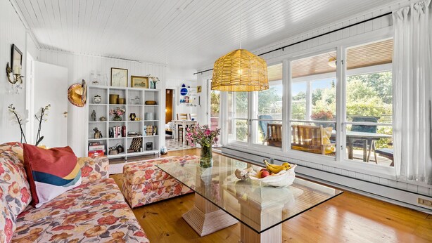 A spacious living room with a glass coffee table, floral sofa, and a large window with a view of the outdoors.