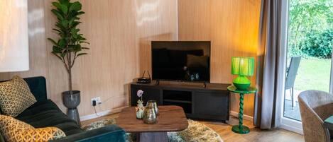 A modern living room with a TV, a green lamp, a potted plant, and a cozy seating area.