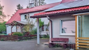Une maison traditionnelle avec un toit recouvert de tuiles rouges, une véranda en bois et un banc à l’extérieur.