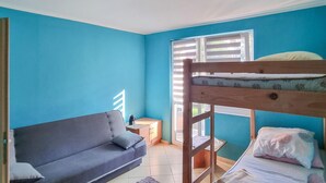 Une pièce avec un lit superposé, un canapé, une petite table et une fenêtre avec des stores.