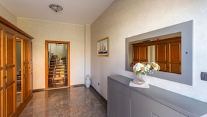 Un couloir avec une porte en bois, un escalier, une armoire grise et un tableau encadré accroché au mur.