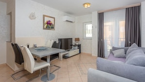 Un salon moderne avec un canapé gris, un coin repas comprenant une table et des chaises, un téléviseur et un tableau accroché au mur.