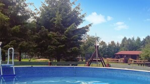 A swimming pool with a wooden swing set and a red-roofed building in the background. - Cozy home in Rekowo with swimming pool (Rekowo)