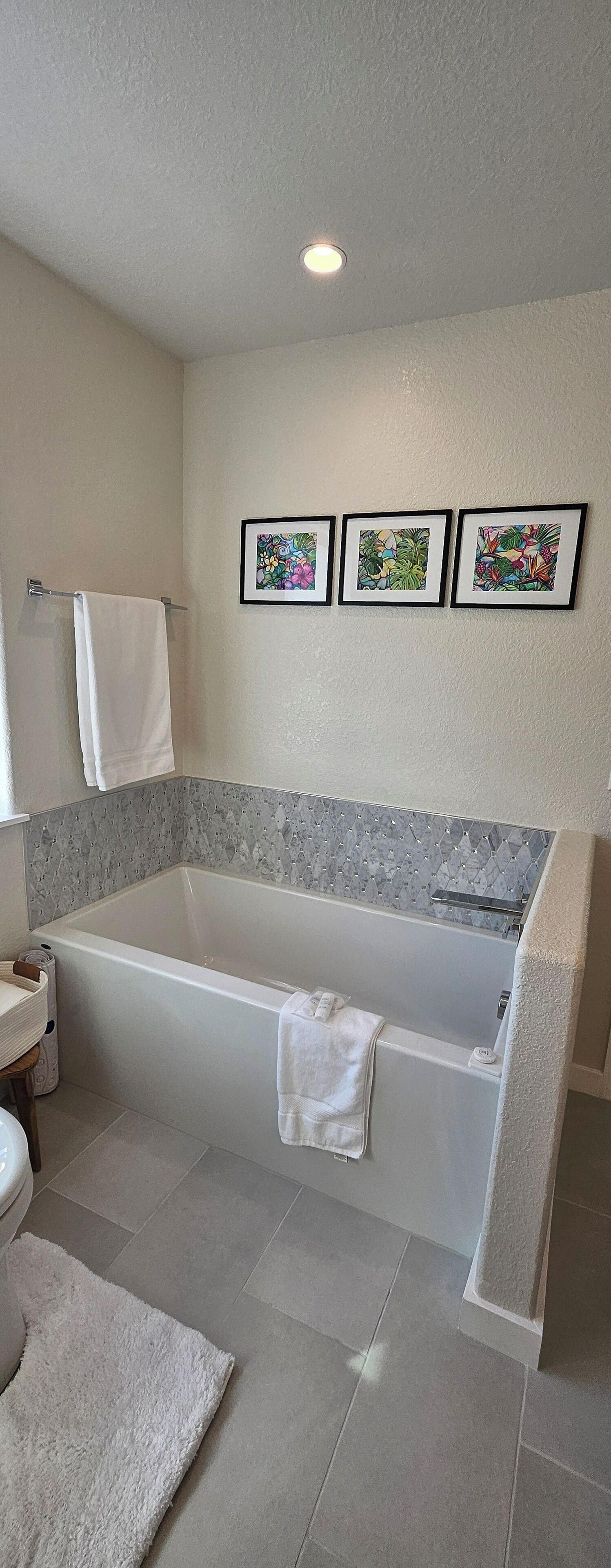 A modern bathroom with a freestanding bathtub, a toilet, and a sink. There are three framed pictures on the wall above the bathtub.