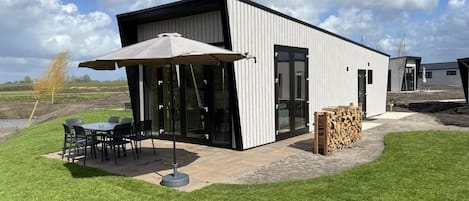 A modern building with a patio area, outdoor seating, and a stack of firewood.
