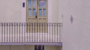 A building facade with a beige door, a small balcony with decorative metal railing, and a textured wall with a decorative tile pattern. - Cozy 1-bedroom suite in amazing Puebla with WiFi and living room with extra bed (Heroica Puebla de Zaragoza)