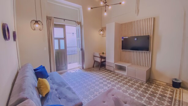 A modern living room with a sofa, a TV mounted on a wooden panel, and a patterned floor. - Cozy 1-bedroom suite in amazing Puebla with WiFi and living room with extra bed (Heroica Puebla de Zaragoza)