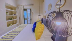 A hotel room with a bed, a shelf with decorative items, a door leading to a bathroom, and a unique hanging light fixture. - Cozy 1-bedroom suite in amazing Puebla with WiFi and living room with extra bed (Heroica Puebla de Zaragoza)
