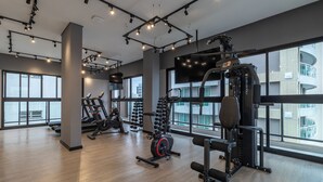 Et moderne fitnesscenter med forskellig træningsudstyr, store vinduer og et højt til loftet.