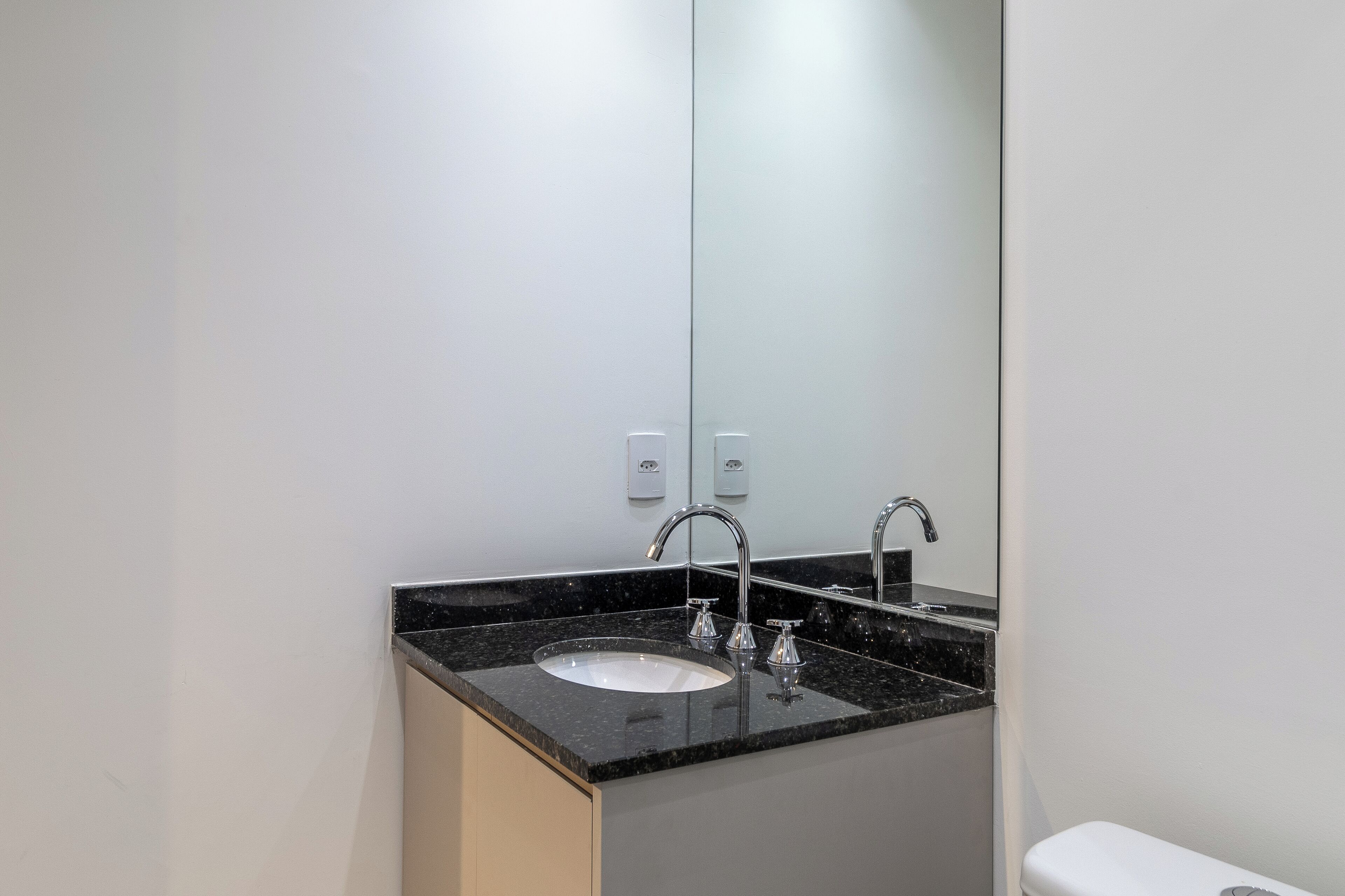 A modern bathroom with a black granite countertop, a white sink, and a large mirror.