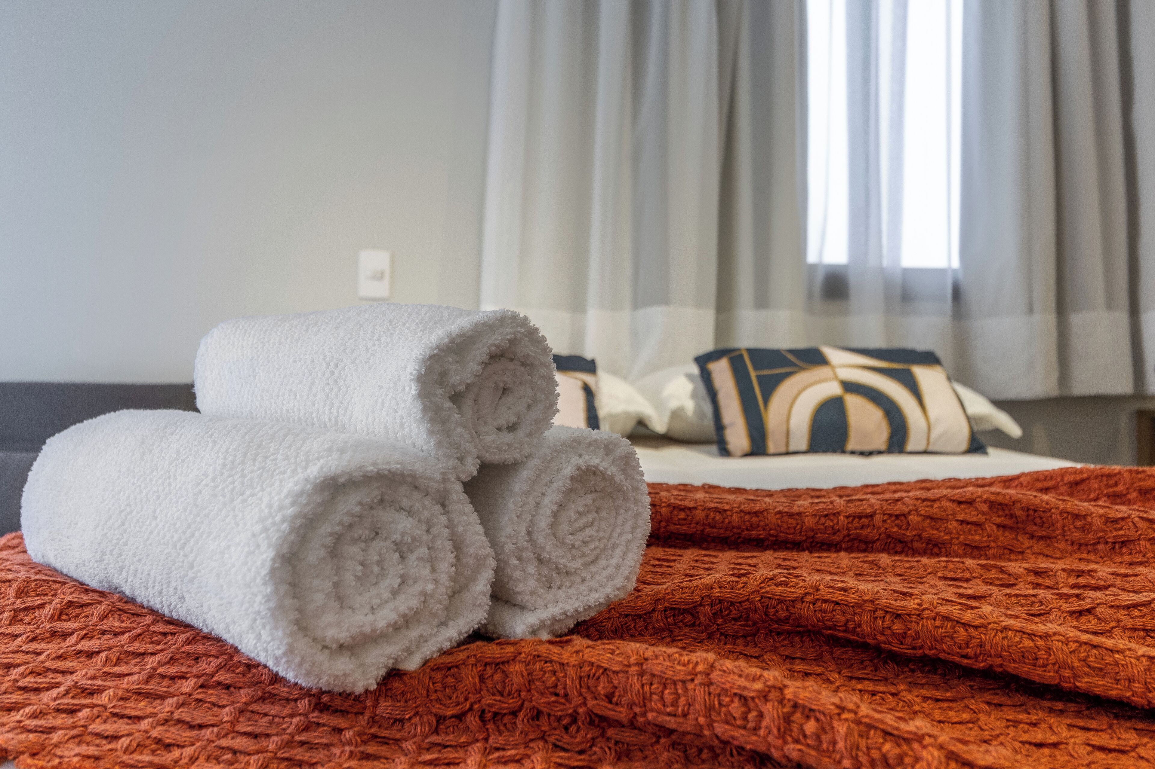A neatly made bed with rolled white towels and a red textured blanket.