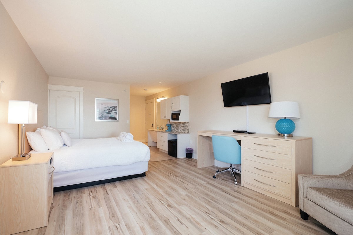 A hotel room with a bed, desk, chair, and a TV on the wall.