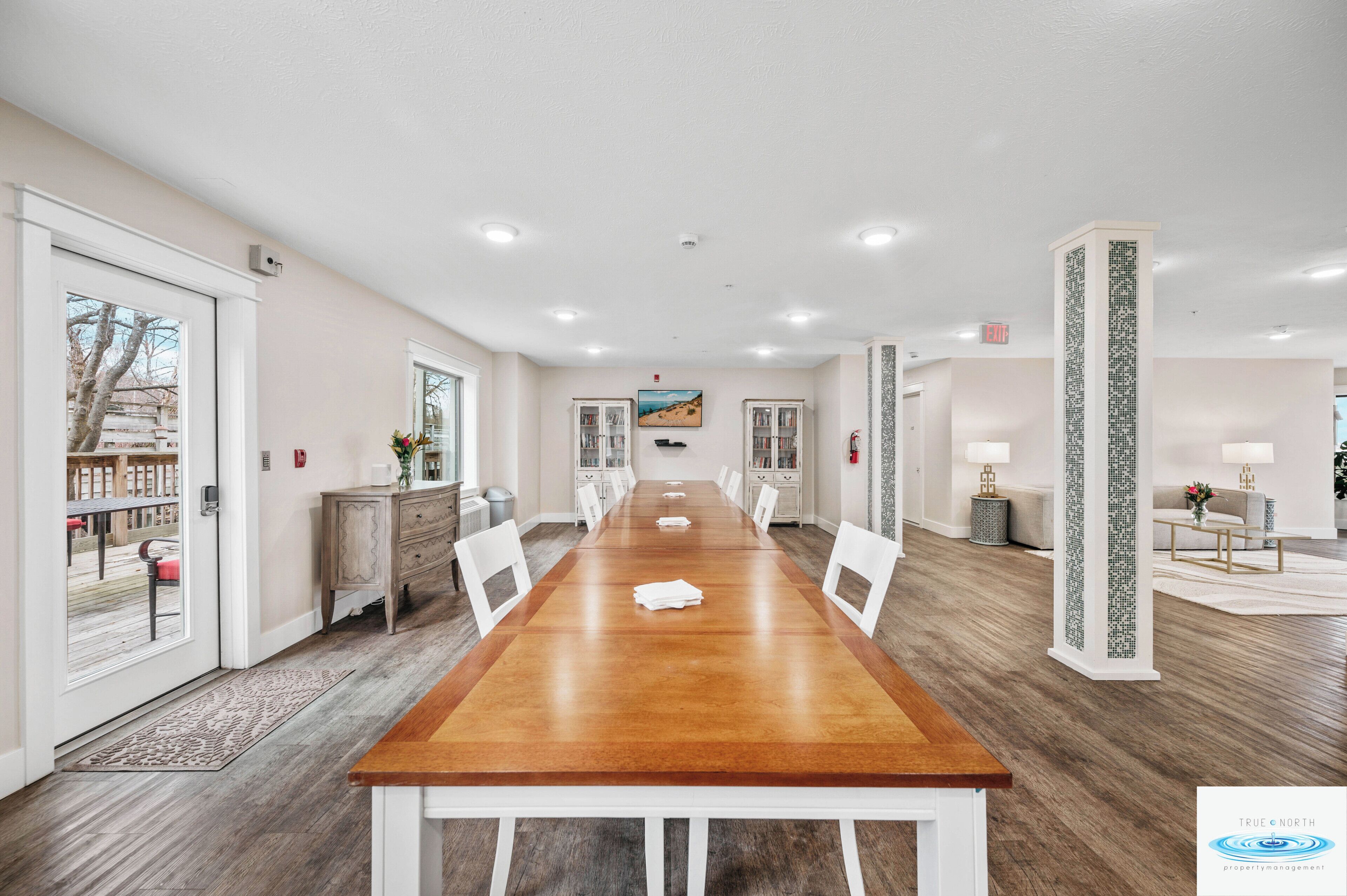 A conference room with a long wooden table, white chairs, and a view of a deck through glass doors.