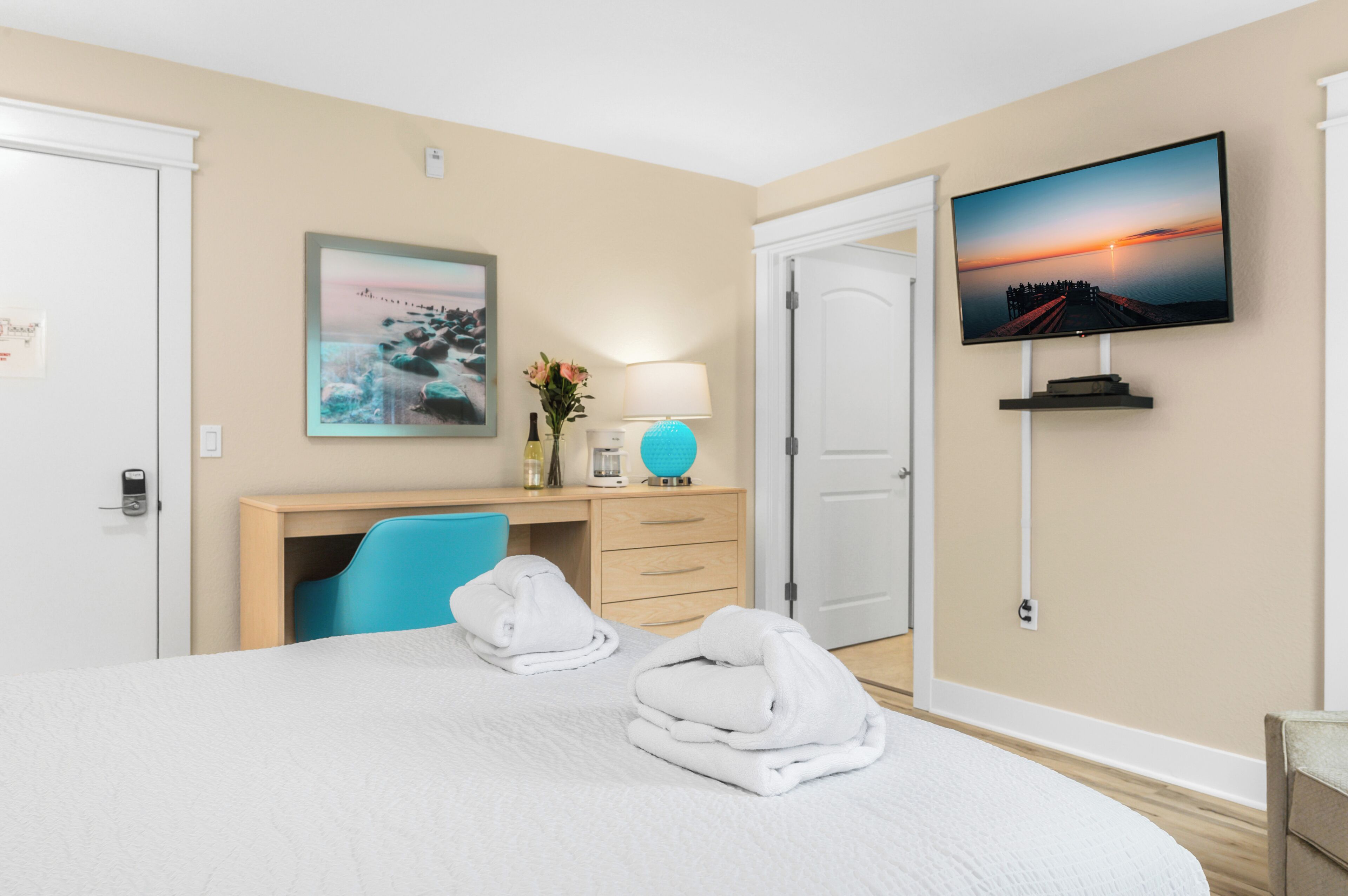 A hotel room with a bed, a desk with a chair, a television, and a door.