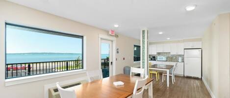 A modern kitchen with a view of the sea, a dining area with a wooden table, and a balcony with a railing.