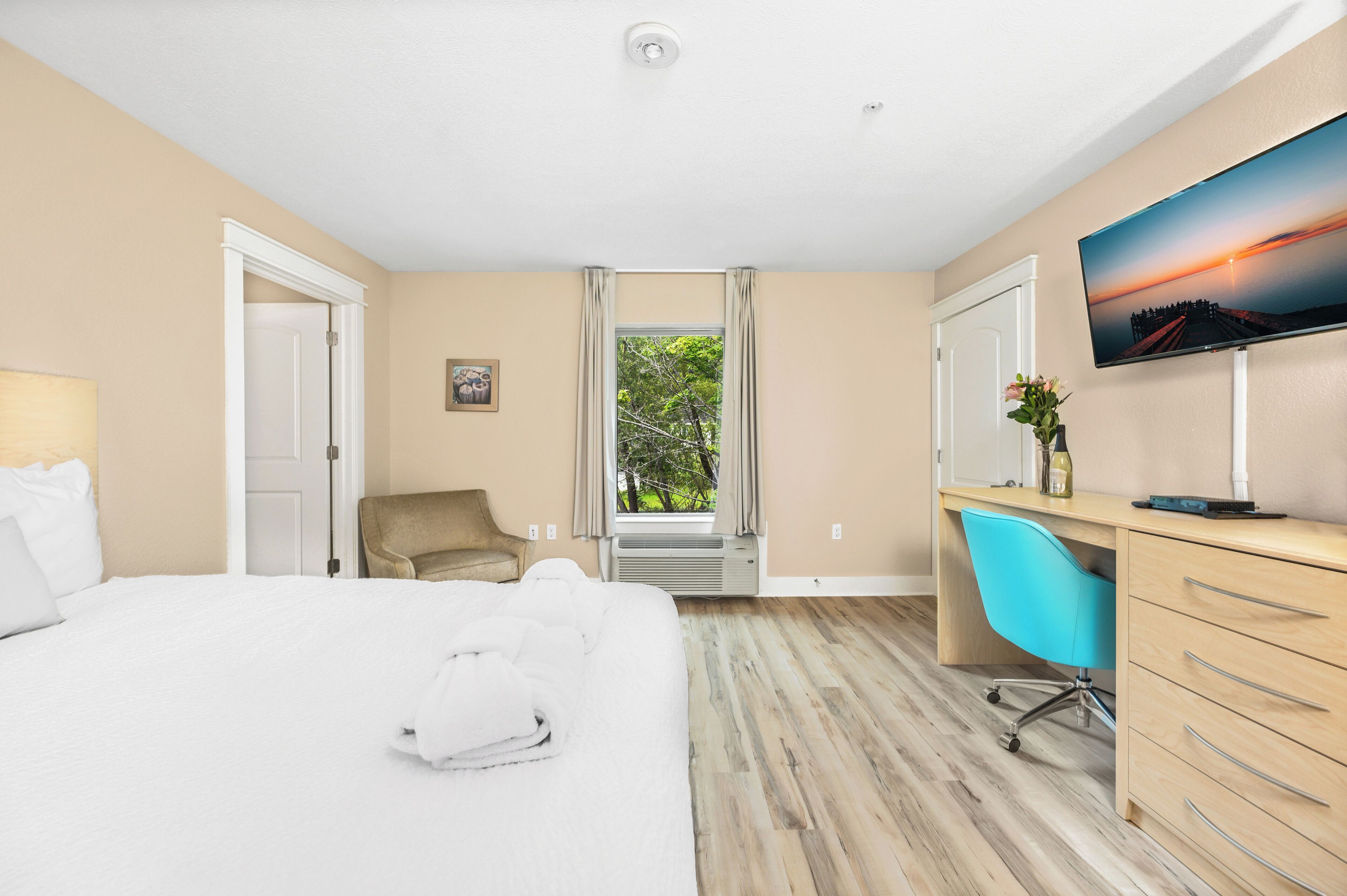 A hotel room with a bed, a desk with a chair, a television, and a window with curtains.