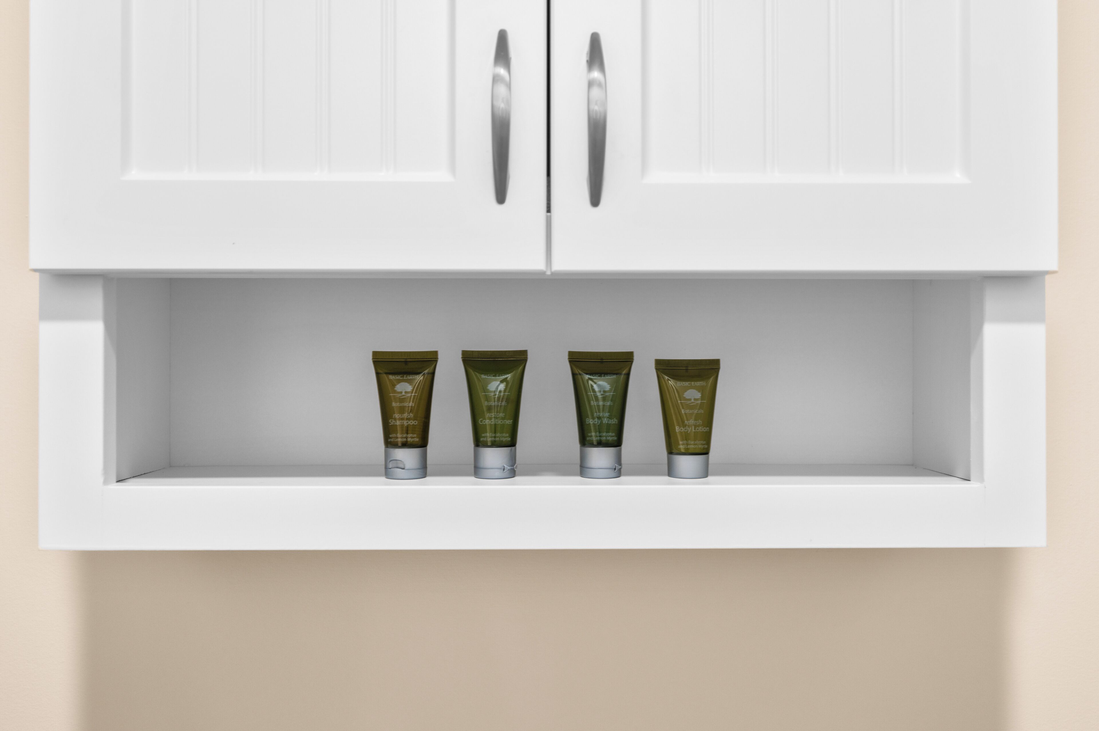 A white cabinet with a shelf below it containing four green bottles.