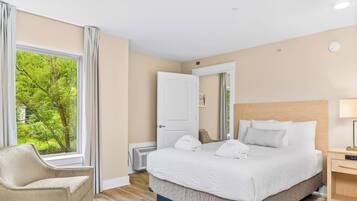A hotel room with a bed, a chair, a bedside table, and a window with a view of trees.
