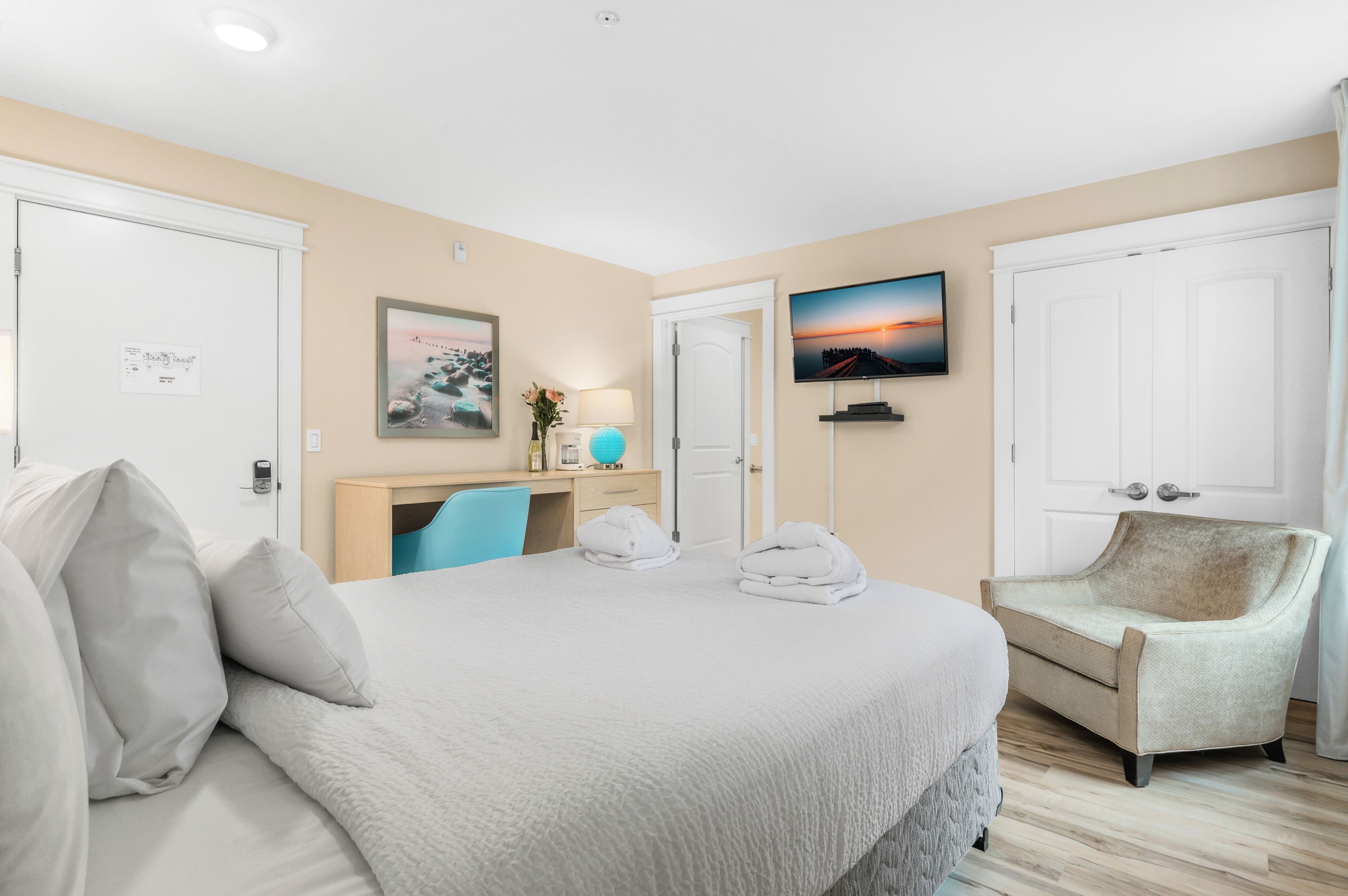 A hotel room with a bed, a desk, a chair, a TV, and a door.