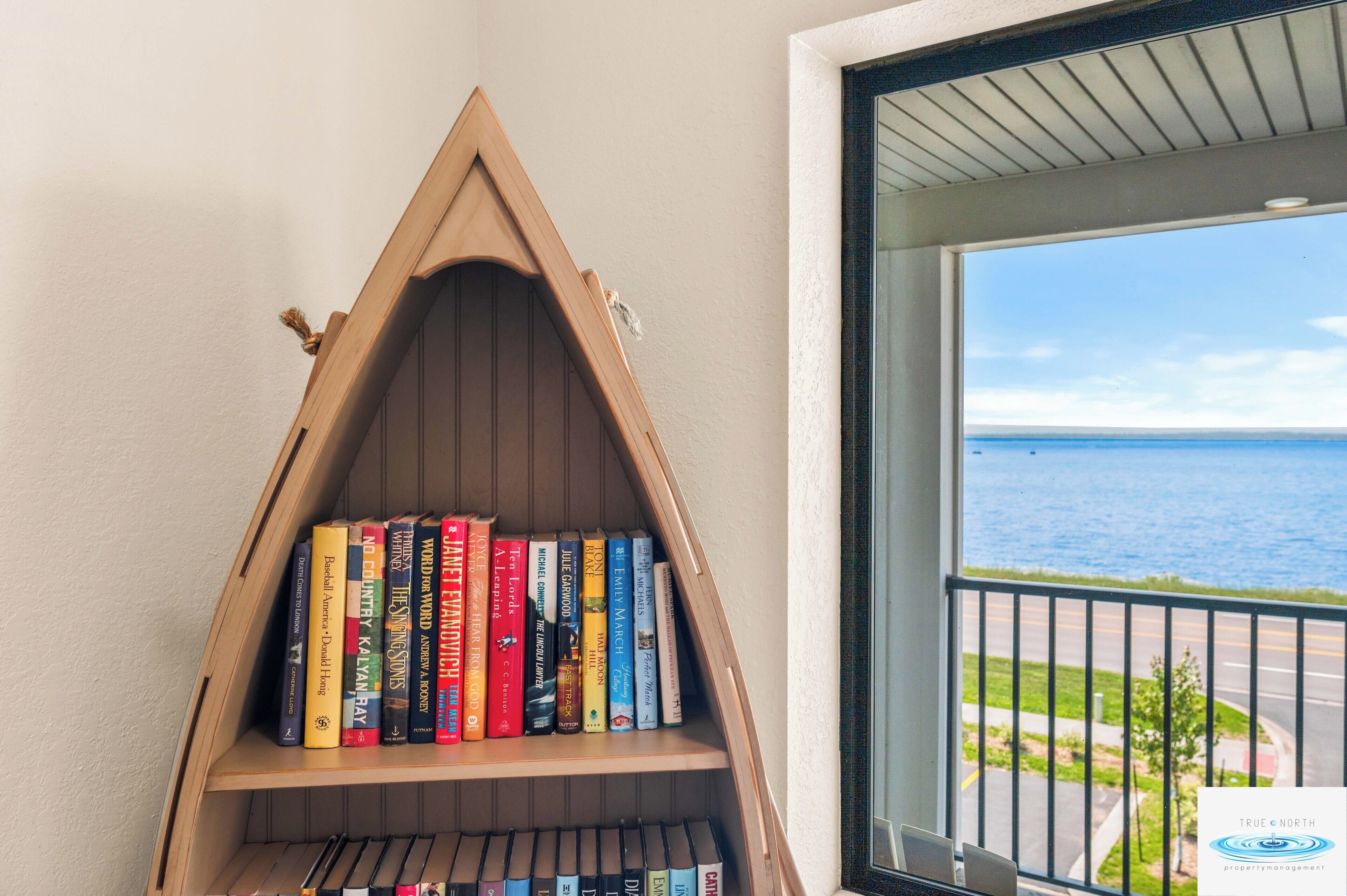A corner bookshelf with books, a balcony with a view of the sea, and a logo for True North Property Management.