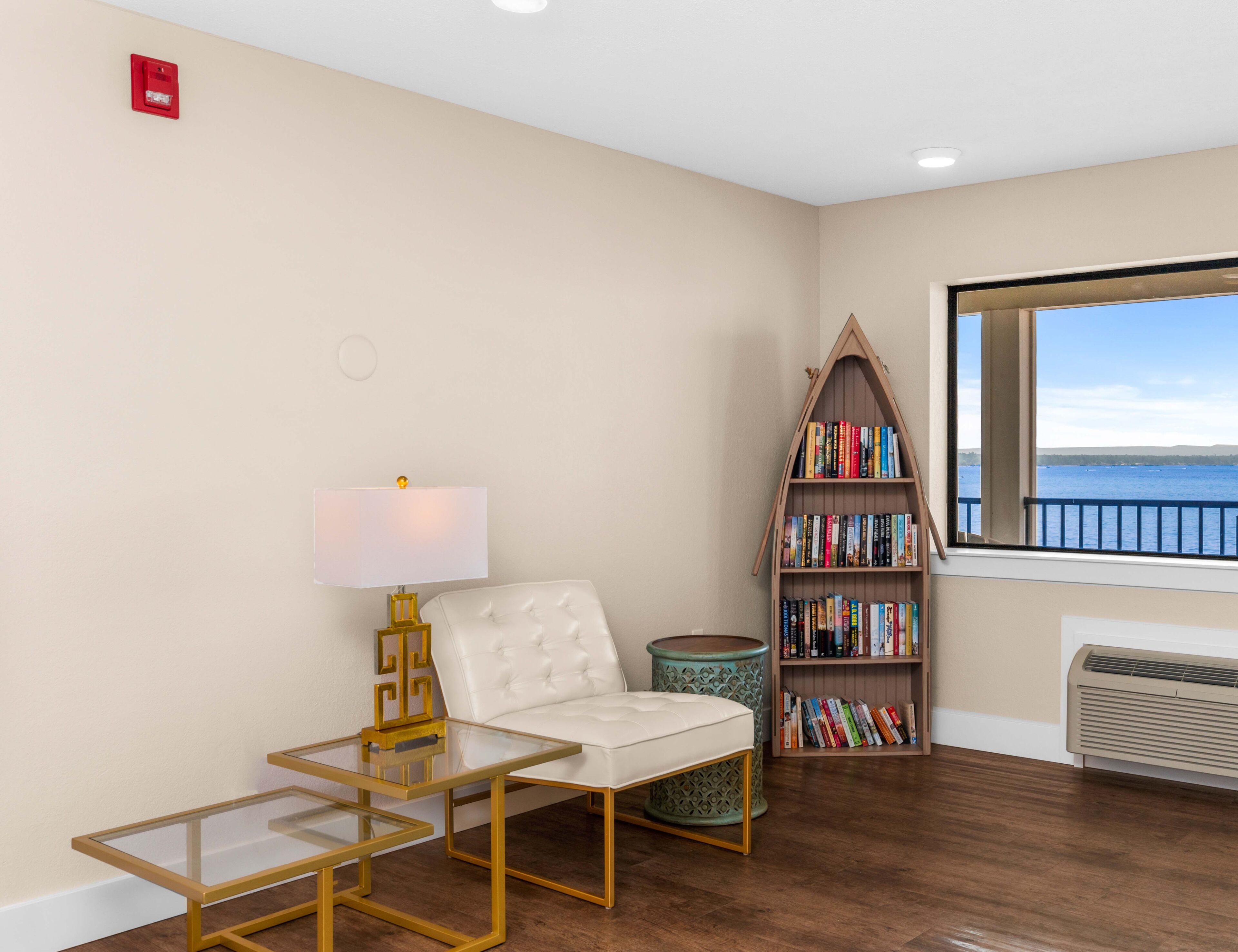 A room with a white sofa, a glass table, a bookshelf, and a view of the sea.