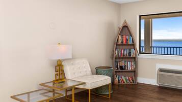 A room with a white sofa, a glass table, a bookshelf, and a view of the sea.