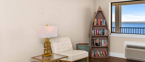A room with a white sofa, a glass table, a bookshelf, and a view of the sea.