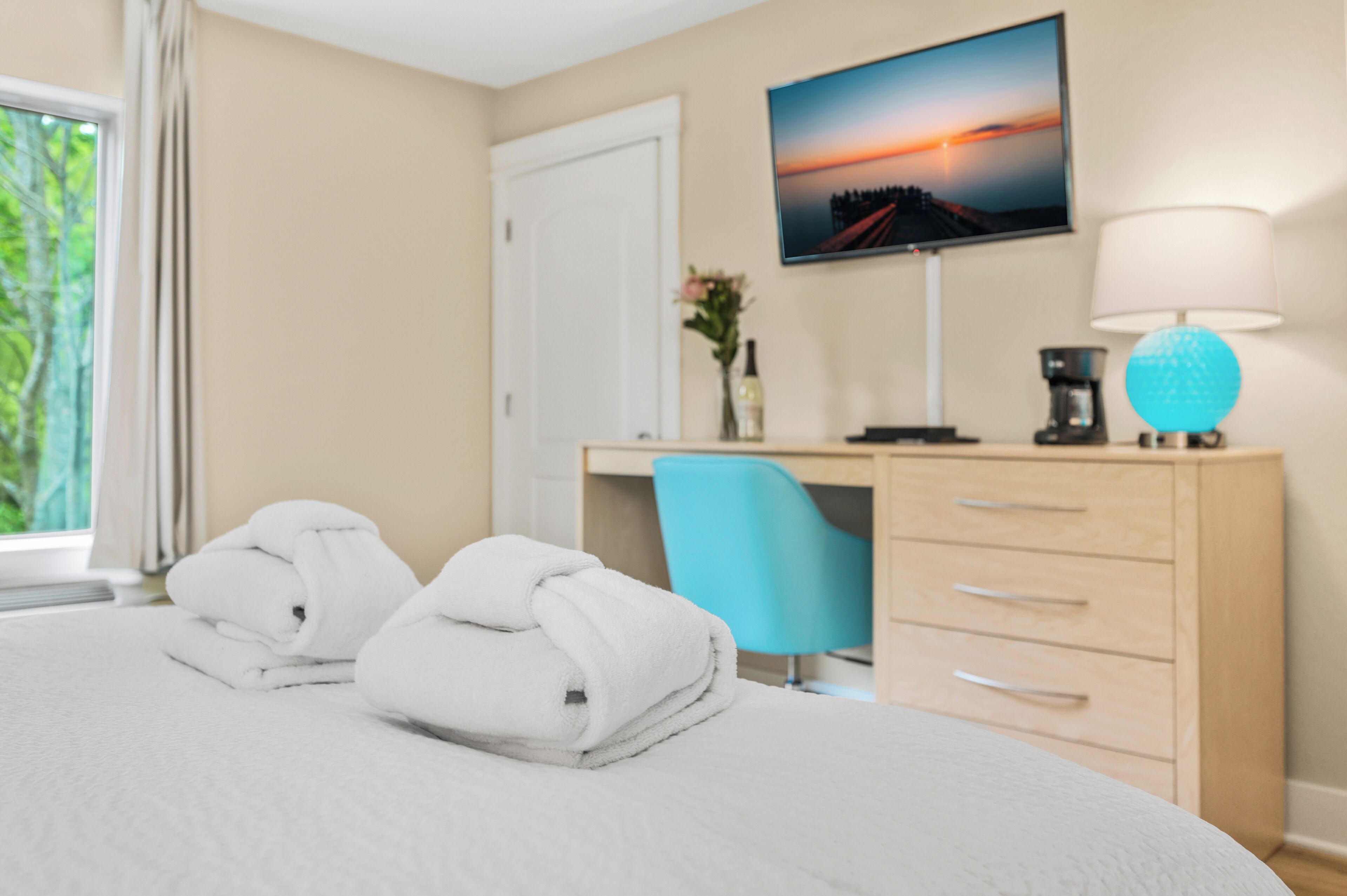 A hotel room with a bed, a desk, a chair, a TV, and a lamp.