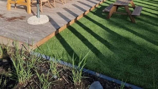 A patio area with wooden tables and chairs, lounge chairs, and a grassy lawn. - Cottage in Zeeland Near the Beach (Koudekerke)